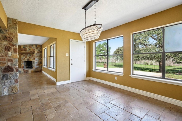 unfurnished dining area featuring baseboards, a textured ceiling, a stone fireplace, and stone tile flooring