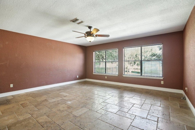 empty room with a ceiling fan, baseboards, visible vents, stone tile flooring, and a textured ceiling