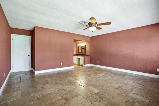 empty room with visible vents, a ceiling fan, a textured ceiling, stone tile flooring, and baseboards