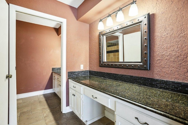 bathroom featuring stone tile flooring, decorative backsplash, baseboards, vanity, and a textured wall