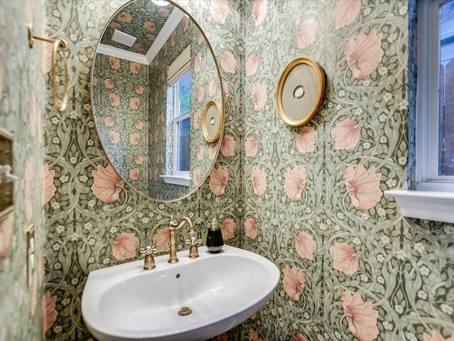 bathroom with wallpapered walls, crown molding, and a sink