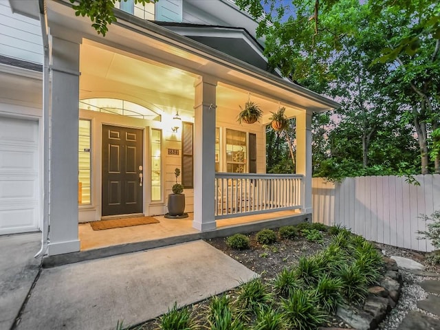 view of exterior entry featuring covered porch, a garage, and fence