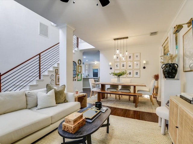 living room featuring visible vents, ceiling fan with notable chandelier, stairway, and dark wood-type flooring