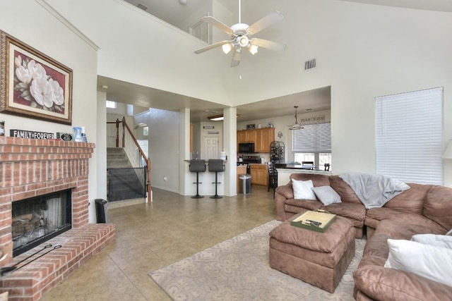 living room with a towering ceiling, stairway, light tile patterned floors, a brick fireplace, and ceiling fan