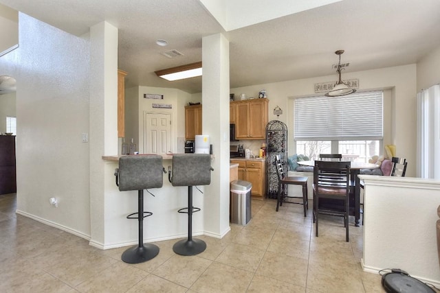 kitchen featuring a breakfast bar, decorative light fixtures, light tile patterned flooring, brown cabinetry, and baseboards