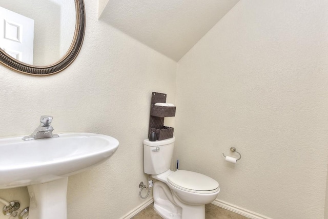 half bath featuring toilet, a textured wall, baseboards, and a sink