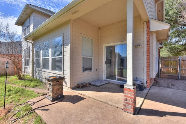 view of exterior entry with a patio and fence