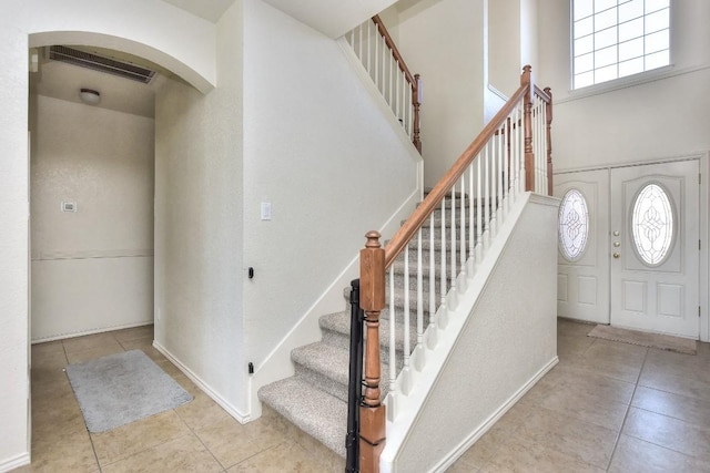 entryway featuring tile patterned flooring, visible vents, stairs, a towering ceiling, and arched walkways