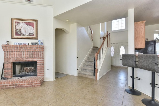 living room with a brick fireplace, baseboards, stairway, light tile patterned floors, and a high ceiling