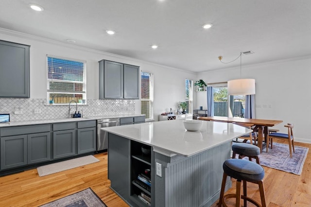 kitchen featuring gray cabinetry, crown molding, dishwasher, a kitchen bar, and a sink