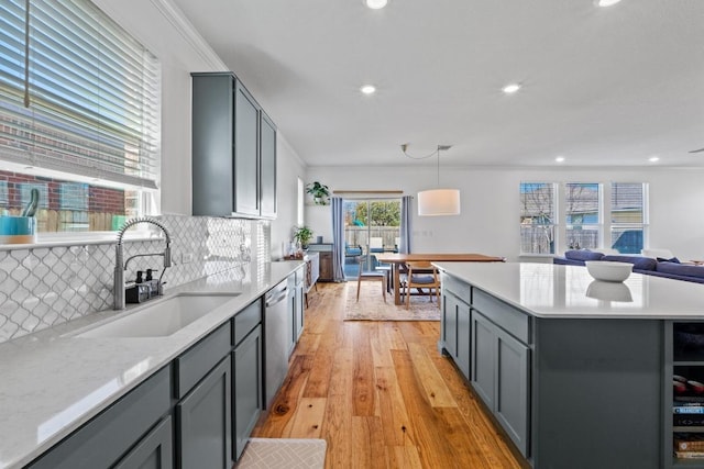 kitchen with light wood-type flooring, gray cabinets, a sink, stainless steel dishwasher, and light countertops