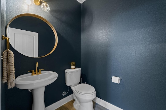 bathroom featuring toilet, wood finished floors, baseboards, and a sink