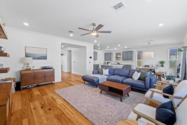 living room featuring arched walkways, visible vents, light wood finished floors, and ornamental molding