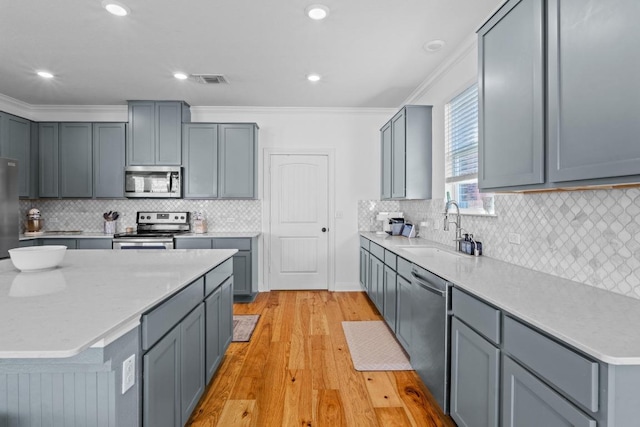 kitchen with visible vents, a sink, appliances with stainless steel finishes, crown molding, and light wood-type flooring