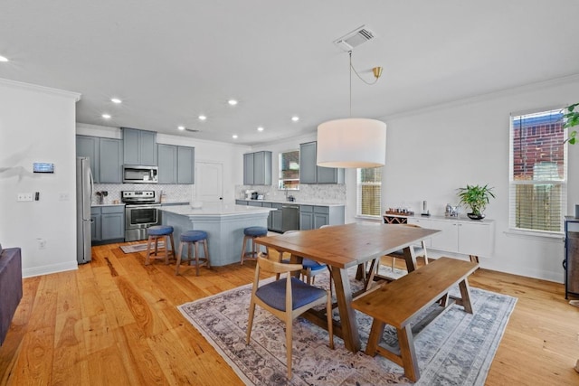 dining area with light wood-type flooring, visible vents, baseboards, and ornamental molding