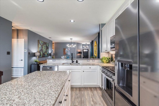 kitchen with light wood-style flooring, a peninsula, white cabinets, stainless steel appliances, and a sink