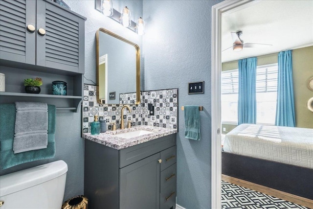 ensuite bathroom with toilet, a ceiling fan, tasteful backsplash, vanity, and a textured wall