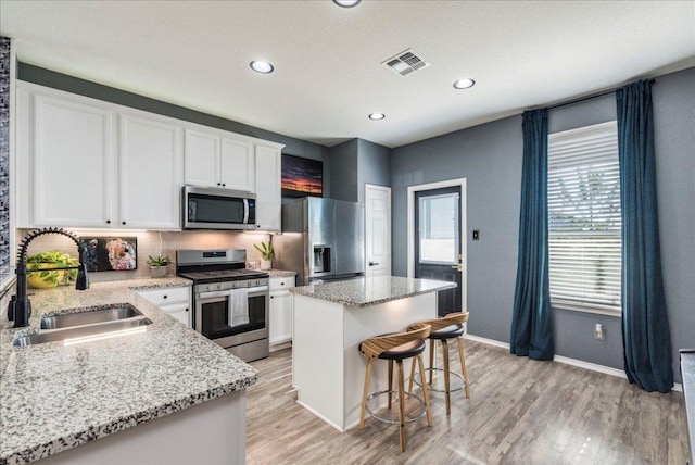 kitchen featuring visible vents, light wood-style flooring, a sink, stainless steel appliances, and a center island