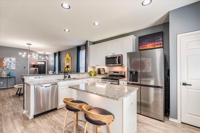 kitchen with a sink, white cabinetry, stainless steel appliances, light wood-style floors, and a peninsula