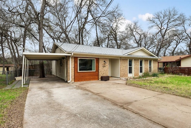 view of front facade with fence, concrete driveway, a shingled roof, a carport, and brick siding