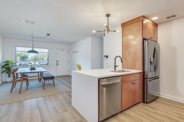 kitchen with visible vents, pendant lighting, light wood-style flooring, appliances with stainless steel finishes, and a sink