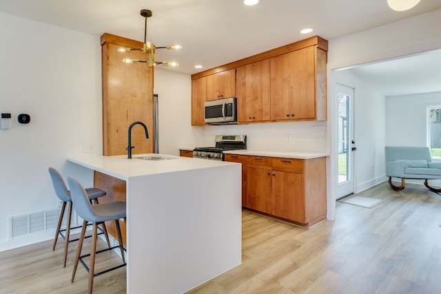 kitchen featuring visible vents, a sink, stainless steel appliances, a breakfast bar area, and light wood finished floors