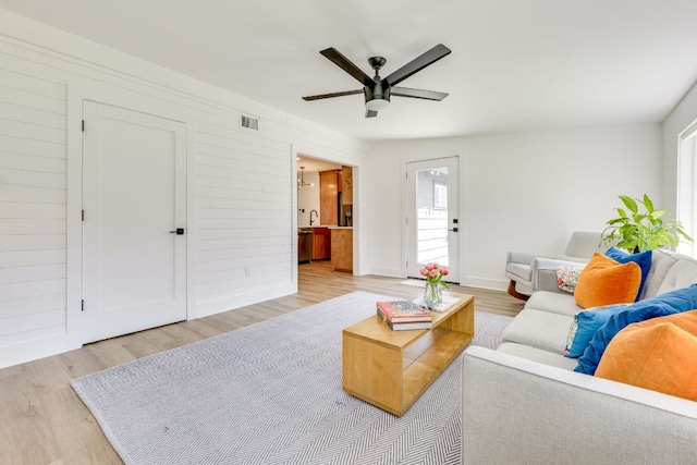 living room with baseboards, wood finished floors, visible vents, and ceiling fan