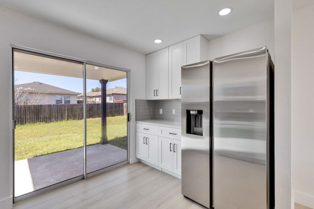 kitchen featuring decorative backsplash, white cabinets, light wood-style flooring, and stainless steel refrigerator with ice dispenser