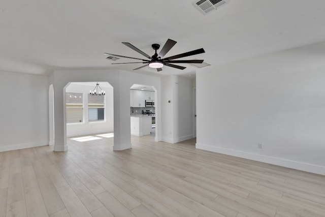 unfurnished living room featuring visible vents, baseboards, arched walkways, light wood-style floors, and ceiling fan with notable chandelier