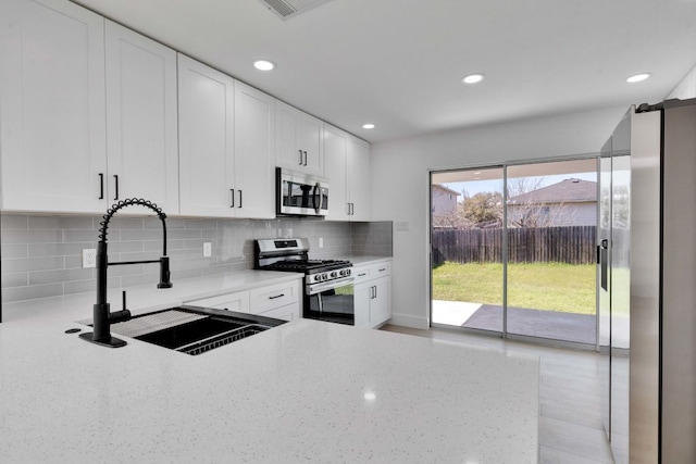 kitchen with light stone countertops, a sink, decorative backsplash, stainless steel appliances, and white cabinetry