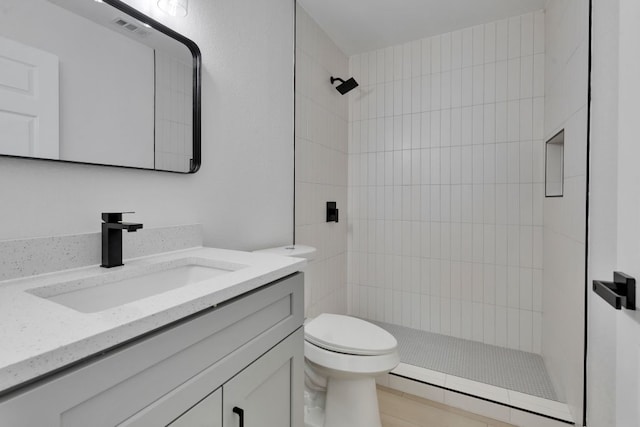 bathroom with visible vents, tiled shower, toilet, and vanity