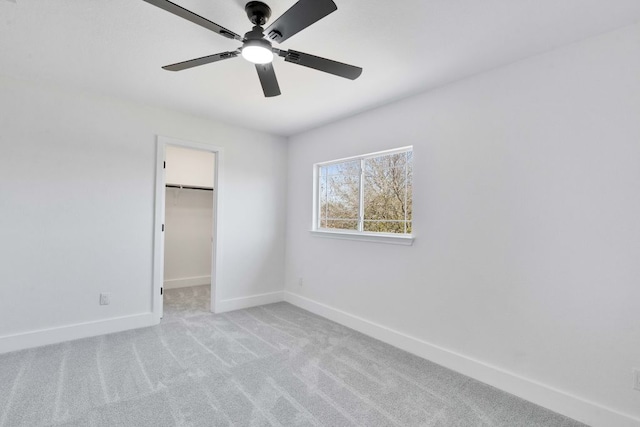 unfurnished bedroom with a spacious closet, ceiling fan, baseboards, light carpet, and a closet