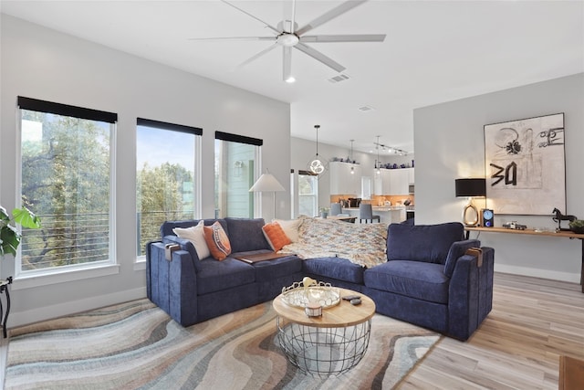 living room with a wealth of natural light, light wood-type flooring, baseboards, and visible vents