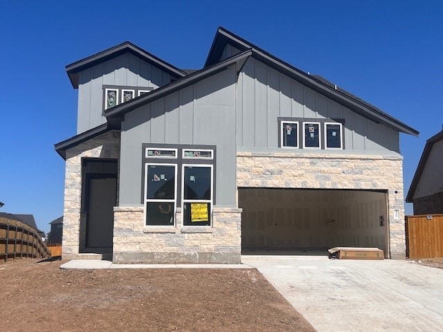 view of front of home with board and batten siding, fence, a garage, stone siding, and driveway