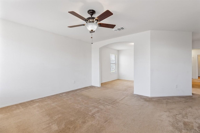 empty room with visible vents, arched walkways, carpet floors, and ceiling fan