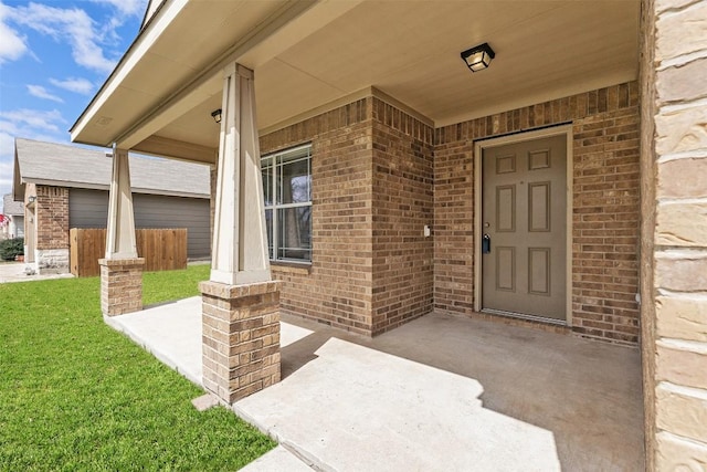 doorway to property featuring brick siding, a porch, and a yard