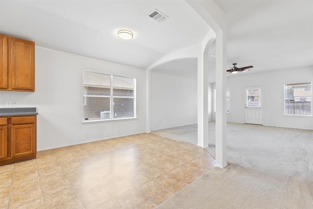 unfurnished living room with visible vents, a ceiling fan, arched walkways, baseboards, and light colored carpet