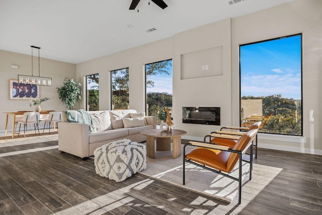 living room with a glass covered fireplace, dark wood-type flooring, a healthy amount of sunlight, and visible vents