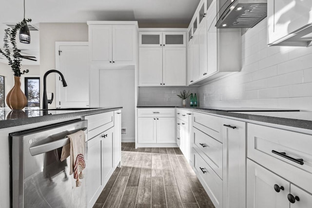 kitchen featuring dark countertops, wood tiled floor, dishwasher, decorative backsplash, and exhaust hood