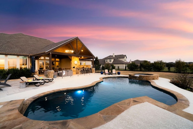 pool at dusk with a patio, a pool with connected hot tub, and outdoor dry bar