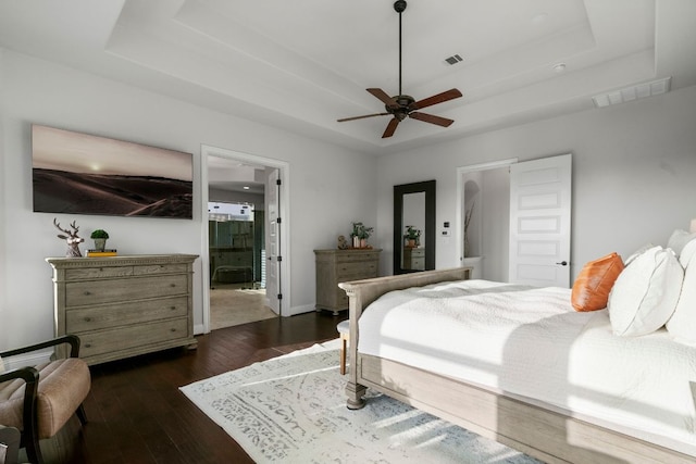 bedroom with visible vents, a raised ceiling, dark wood-style floors, and ensuite bathroom