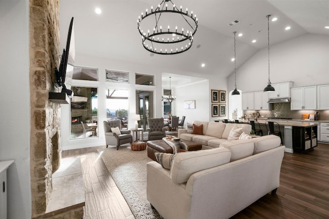 living room featuring high vaulted ceiling, dark wood-style floors, recessed lighting, an inviting chandelier, and a fireplace