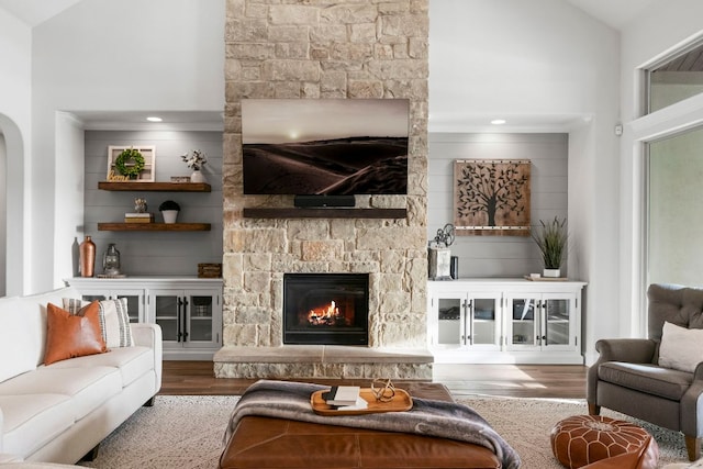 living area with arched walkways, high vaulted ceiling, wood finished floors, and a fireplace