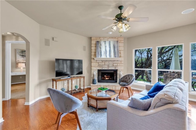 living area featuring baseboards, ceiling fan, a fireplace, wood finished floors, and arched walkways