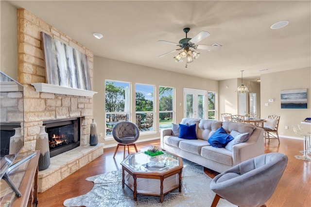 living room featuring baseboards, a stone fireplace, wood finished floors, and a ceiling fan