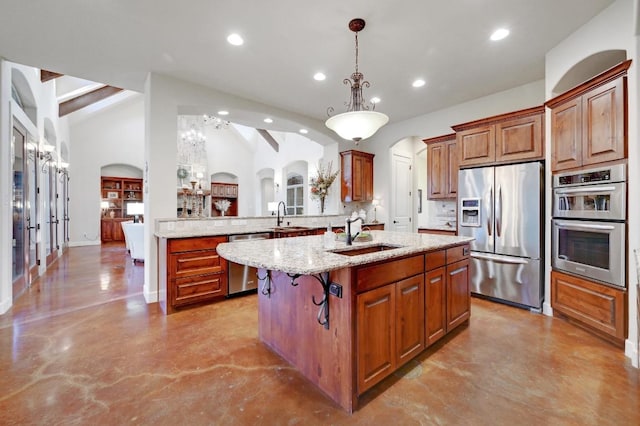 kitchen featuring light stone counters, a center island with sink, arched walkways, a sink, and appliances with stainless steel finishes