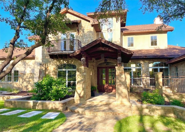 23923 Tres Coronas, Spicewood, TX 78669 - view of front of property featuring stone siding, a balcony, french doors, a chimney, and stucco siding