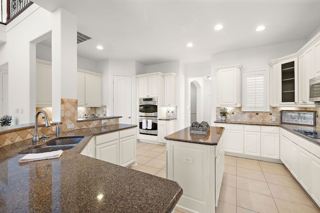 kitchen with a sink, a kitchen island, stainless steel appliances, arched walkways, and light tile patterned floors