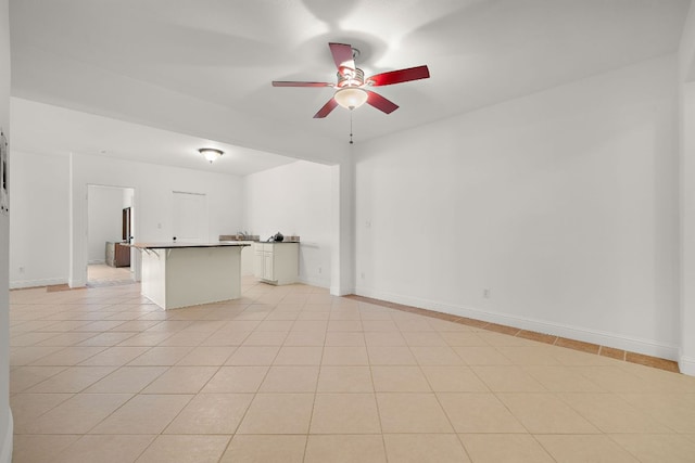 interior space with light tile patterned floors, a ceiling fan, and baseboards