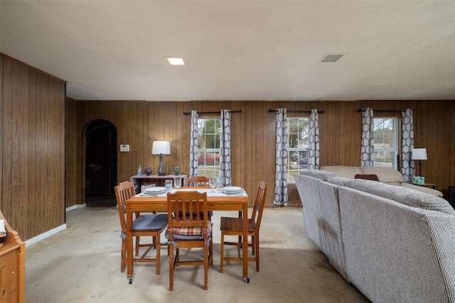 dining room featuring wooden walls, plenty of natural light, light colored carpet, and arched walkways